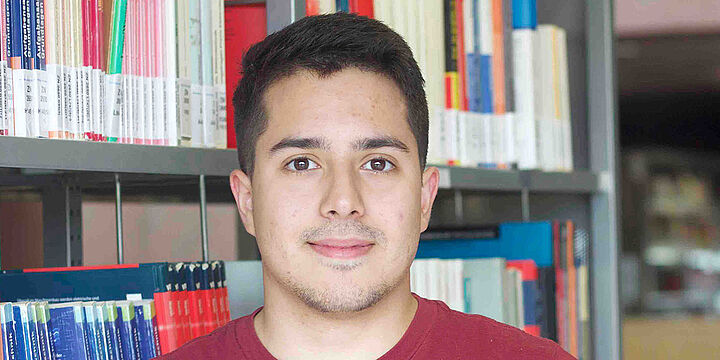 Automatisierungstechnik Junger Mann mit rotem Shirt steht vor einem Bücherregal
