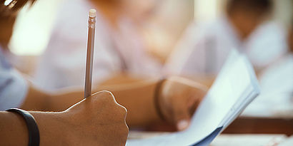 Person sitzt am Tisch und schreibt etwas mit einem Stift