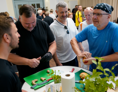 Menschen schneiden Obst und Gemüse an einem Stehtisch