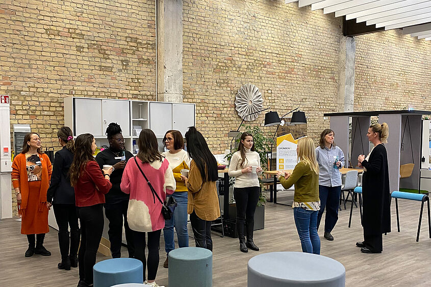 Women for Excellence Personen stehen in einer größeren Gruppe zusammen und sind miteinander im Gespräch.