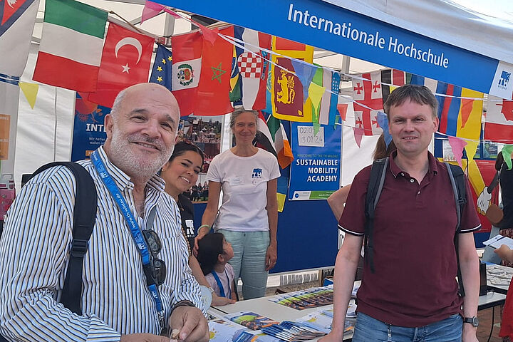 Vier Personen schauen in die Kamera, umgeben von internationalen Flaggen