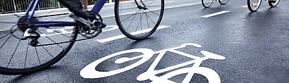 Asphaltierte Straße mit Fahrradsymbol und Radfahrenden, die vorbeifahren