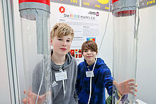 Zwei Kinder halten große zwei große durchsichtige Behälter in die Kamera