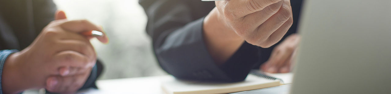 Nahaufnahme auf Hände zweier Personen, die am Schreibtisch mit Laptop arbeiten.