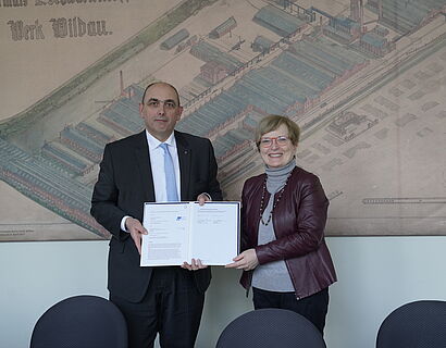 Prof. Ulrike Tippe und RKI-Präsident halten Kooperationsvereinbarung in der Hand und lächeln in die Kamera