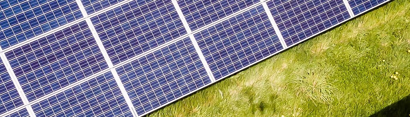 Schrägansicht von Solarmodulen, die über einer grünen Wiese positioniert sind.