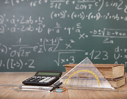 Tafel mit Mathematikformeln und Matheutensilien auf dem Tisch