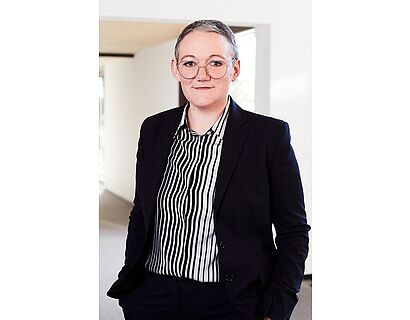 Medium Shot-Fotografie von Judith Muster in dunklem Anzug, die Hände in den Hosentaschen.