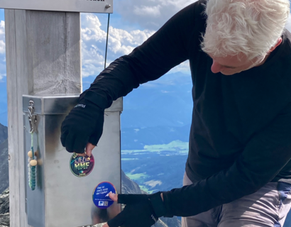 Person klebt Sticker an ein Gipfelkreuz