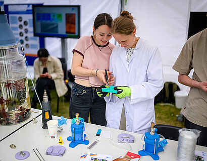 Zwei Personen stehen an einem Info-Stand beim HIT 2026 und schneiden etwas zurecht