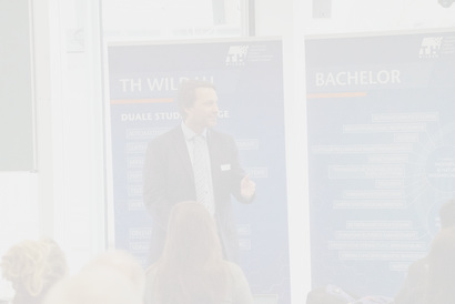 Hier ist eine Person vor blauen Aufstellern zu sehen, die einen Vortrag vor Menschen hält.