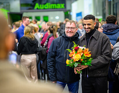Zwei Männer stehen zusammen, einer hält einen Blumenstrauß und beide lächeln in die Kamera