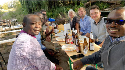 Eine Gruppe von Personen sitzt gemeinsam an einer langen Biertischgarnitur im Freien und lächelt in die Kamera.