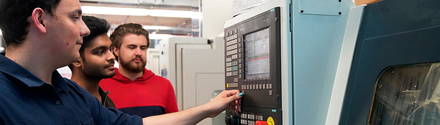 Drei Studierende bedienen in einem Maschinenbau-Labor eine große Maschine