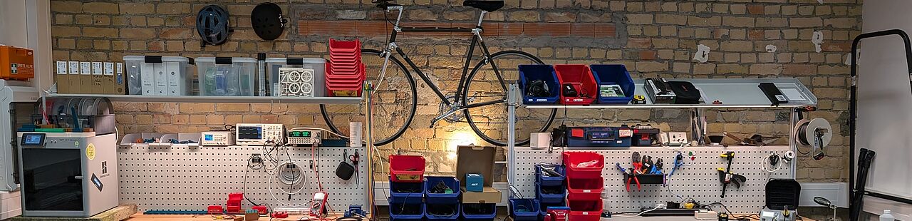 Werkbank mit verschiedenen Utensilien und einem Fahrrad an einer Backsteinwand im Hintergrund