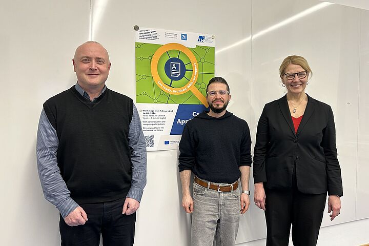 Dr. Markus Karbaum, Ray Trautwein und Katrin Gebhardt stehen vor dem Plakat der Career. Application. Week im Februar 2026