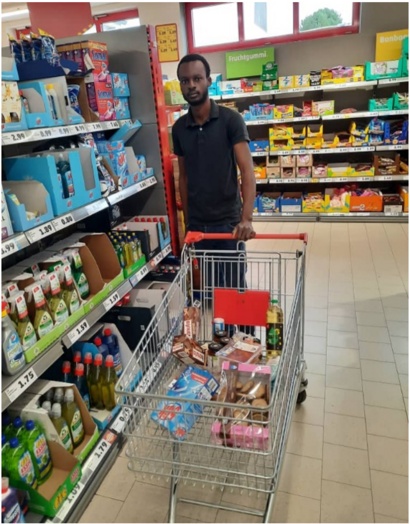 Ein junger Mann mit einem Einkaufswagen steht in einem Supermarkt vor einem Verkaufsregal.