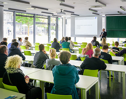 Studieninteressierte in einem Seminarraum hören einem Professor zu
