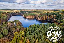 Der Paul-Gerhardt-Weg von Berlin nach Lübben durch das Dahme-Seenland ist als einziger Wanderweg Brandenburgs für den Titel „Deutschlands schönster Wanderweg 2024“ nominiert. (Bild: Michael Zalewski / Landkreis Dahme-Spreewald) Der Paul-Gerhardt-Weg von Berlin nach Lübben durch das Dahme-Seenland, Luftbild mit Seenlandschaft und Logo