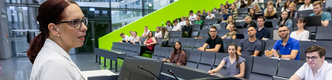 Eine Professorin hält in einem vollen Hörsaal eine Vorlesung.