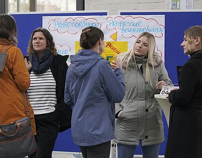 Drei Mitarbeiterinnen des Karrierezentrums unterhalten sich am Präsentationsstand mit Hochschulangehörigen.