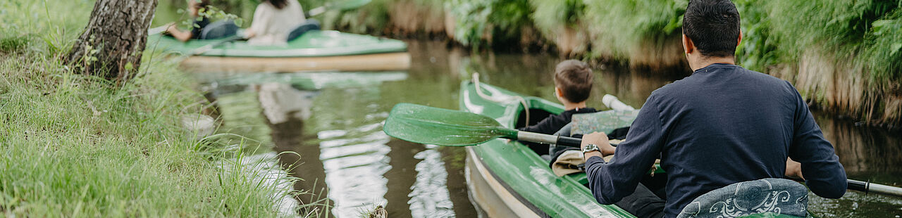 Kajak mit einer Person fährt auf dem Wasser, einem schmalen Kanal, durch eine Waldlandschaft