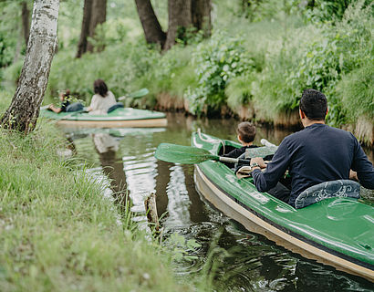 Kajak mit einer Person fährt auf dem Wasser, einem schmalen Kanal, durch eine Waldlandschaft