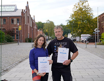 Zwei Wander/-innen mit Urkunde auf dem Campus der TH Wildau