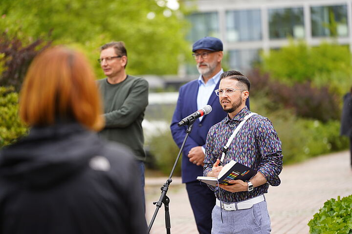 Man sieht Ray Trautwein, Frank Nerlich und Thomas Lehne bei den Reden vor Haus 13 im Rahmen des Hissens der Regenbogenfahne beim Deutschen Diversity-Tag 2025.