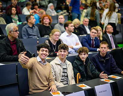 Absolvent*innen bei der Verabschiedung 2025 machen ein Selfie im Audimax