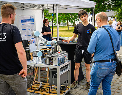 Drei Personen stehen um einen Greifarm-Roboter beim HIT 2026 