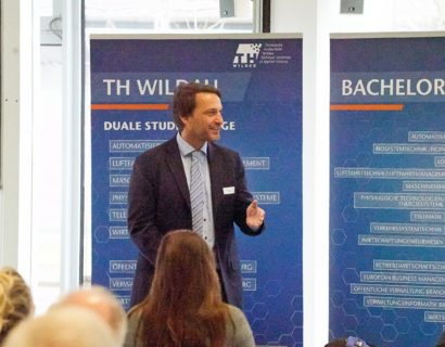 Prof. Stollhoff beim Netzwerktreffen Duales Studium Ein Mann steht vor Roll-Up Postern und hält einen Vortrag