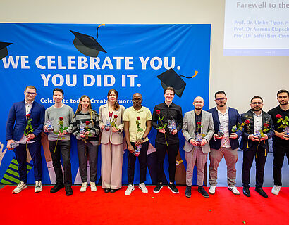 Absolvent*innen stehen bei der Verabschiedung 2025 für ein Gruppenfoto in einer Reihe