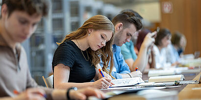 Studierende sitzen am Tisch in der Bibliothek und schauen in ihre Bücher