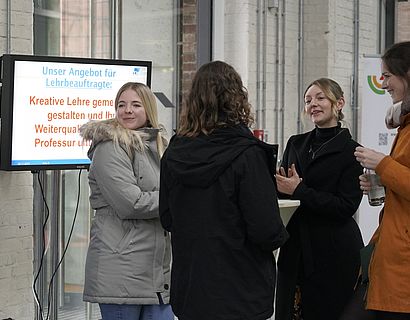 Mitarbeiterinnen des Karrierezentrums unterhalten sich am Präsentationsstand mit Hochschulangehörigen.