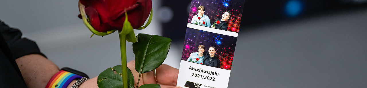 Absolventin hält Rose und Bilder von der Verabschiedung 2022 in die Kamera