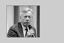 Prof. Andreas Paul Timmermann Schwarz-weiß Portrait eines Mannes mit einem Mikrofon in der Hand auf grauem Hintergrund