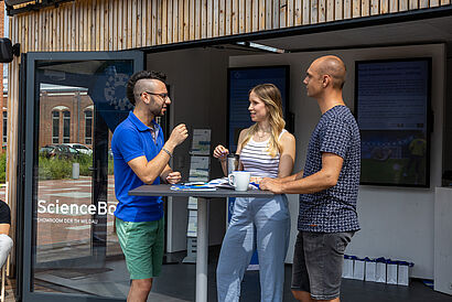 Drei Studierende stehen an einem Stehtisch vor der ScienceBox auf dem Campus der TH Wildau