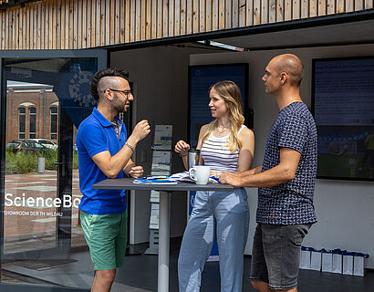 Drei Studierende stehen an einem Stehtisch vor der ScienceBox auf dem Campus der TH Wildau