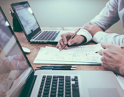 zwei MacBooks und zwei Partner, die miteinander eine Problemlösung entwickeln