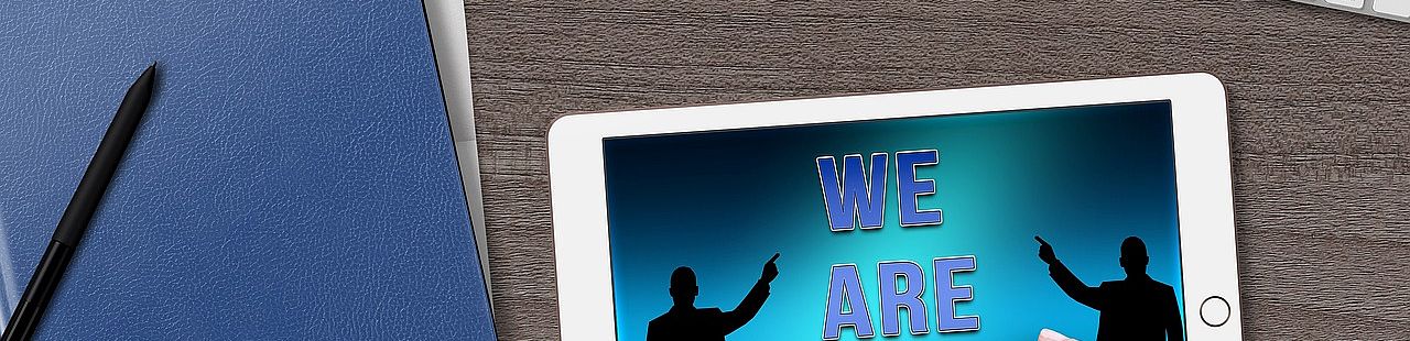Tastatur, Kaffeetasse, Block mit Stift und Tablet mit Aufschrift "We are hiring" auf dem Tisch