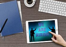 Recruiting Tastatur, Kaffeetasse, Block mit Stift und Tablet mit Aufschrift "We are hiring" auf dem Tisch