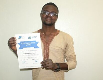 Ein Wissenschaftler hält lächelnd eine Urkunde für den „Young Researcher Award“ in die Kamera.