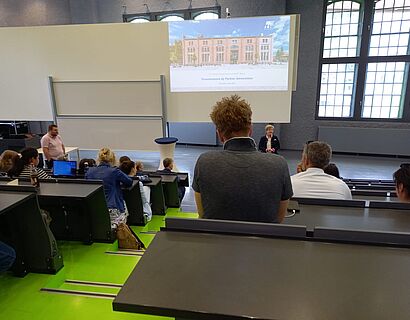 Menschen sitzen in einem Hörsaal und schauen sich - von hinten fotografiert - eine Präsentation an