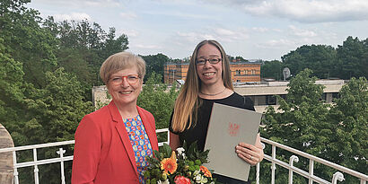 TH-Wildau-Präsidentin Prof. Ulrike Tippe gratuliert Prof. Lydia Göse zum Landeslehrpreis 2024, die einen Blumenstrauß und die Urkunde in der Hand hält. 