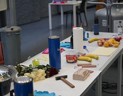 Kinderuni Winter Edition 2024 - diverse Hilfsmittel und Zutaten für ein Experiment, unter anderem ein Hammer, Bananen und Rosen