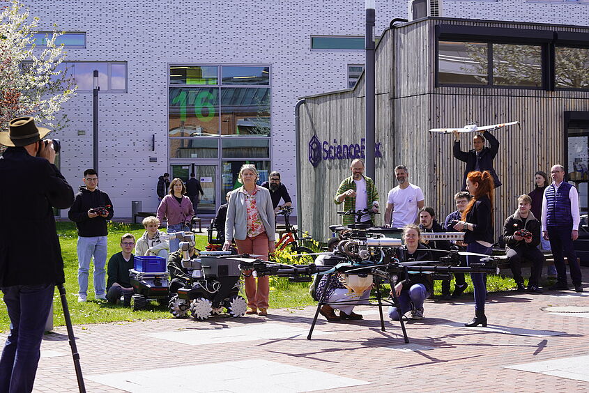 Personen stehen mit Flugobjekten, darunter Drohnen, auf dem Campus der TH Wildau und werden fotografiert