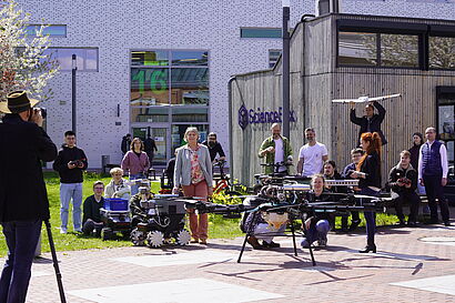 Personen stehen mit Flugobjekten, darunter Drohnen, auf dem Campus der TH Wildau und werden fotografiert
