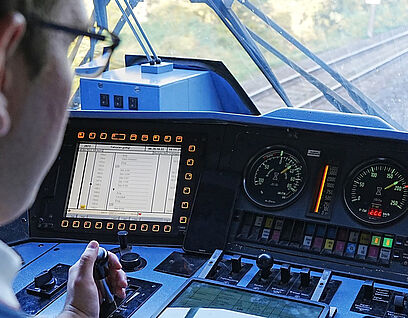 Ein Zugführer von hinten fotografiert bei der Arbeit im Zug mit der Hand am Steuerhebel
