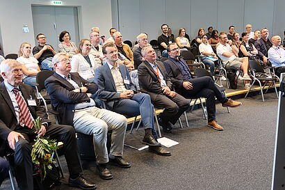 Zahlreiche Personen sitzen bei einer Jubiläumsveranstaltung auf Stühlen und schauen nach vorn